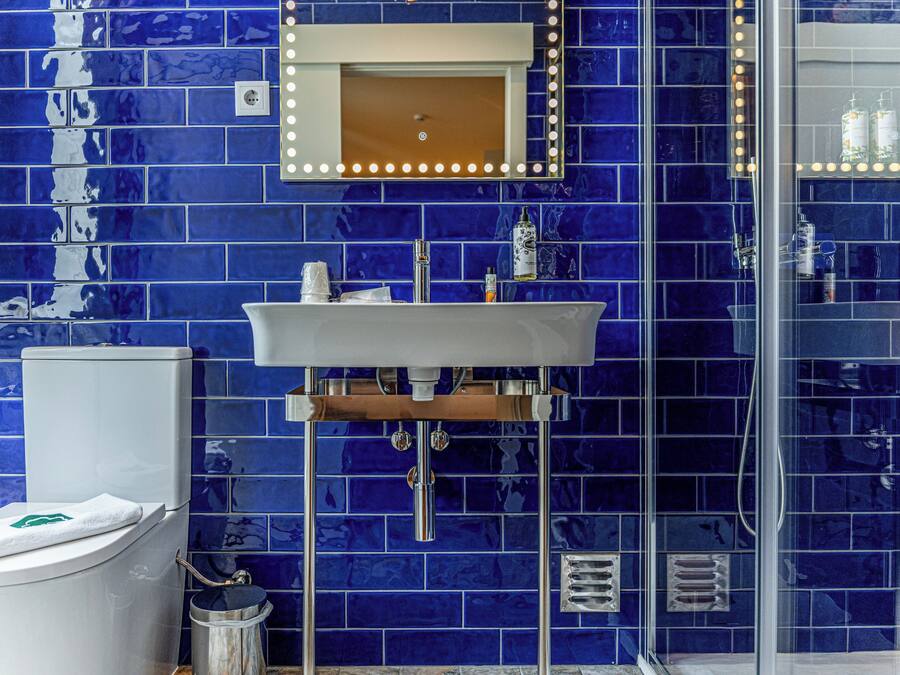 A bathroom with a blue-tiled wall, a white sink, a mirror with lights, and a glass shower enclosure.