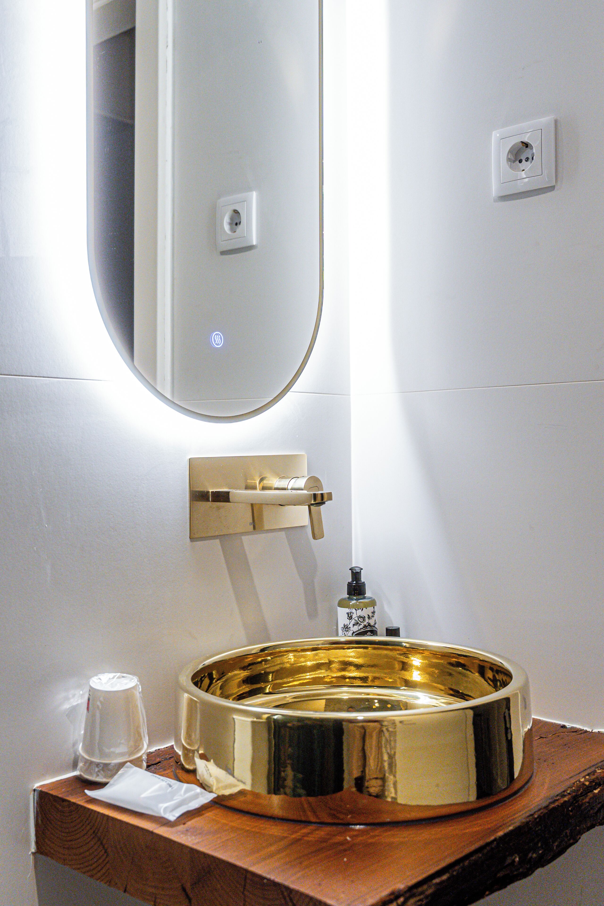 Un baño con un lavamanos dorado, un espejo y un dispensador de jabón.