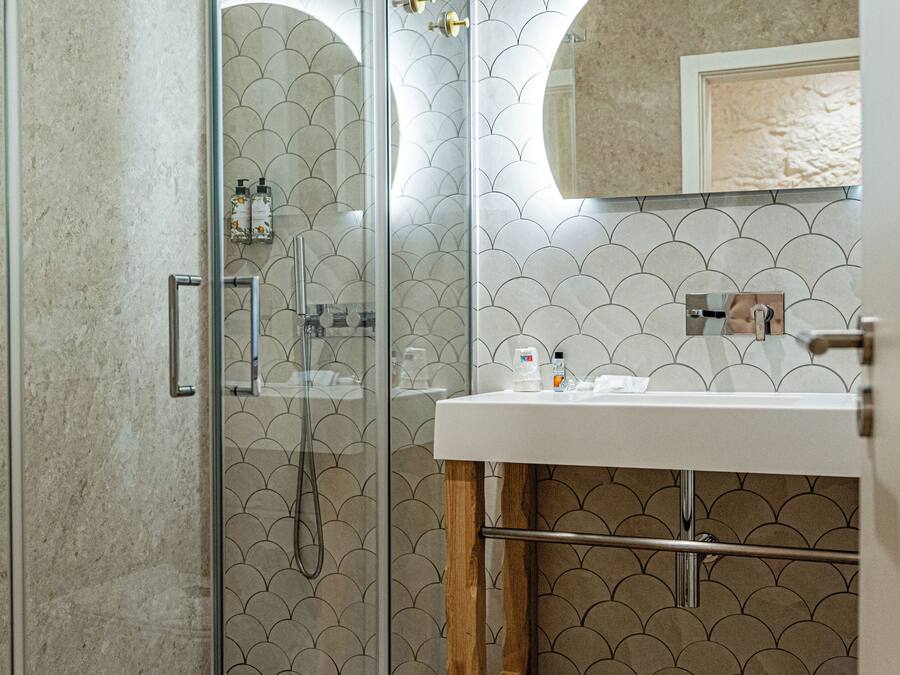 A modern bathroom with a glass-enclosed shower, a white sink, and a tiled wall with a scalloped pattern.
