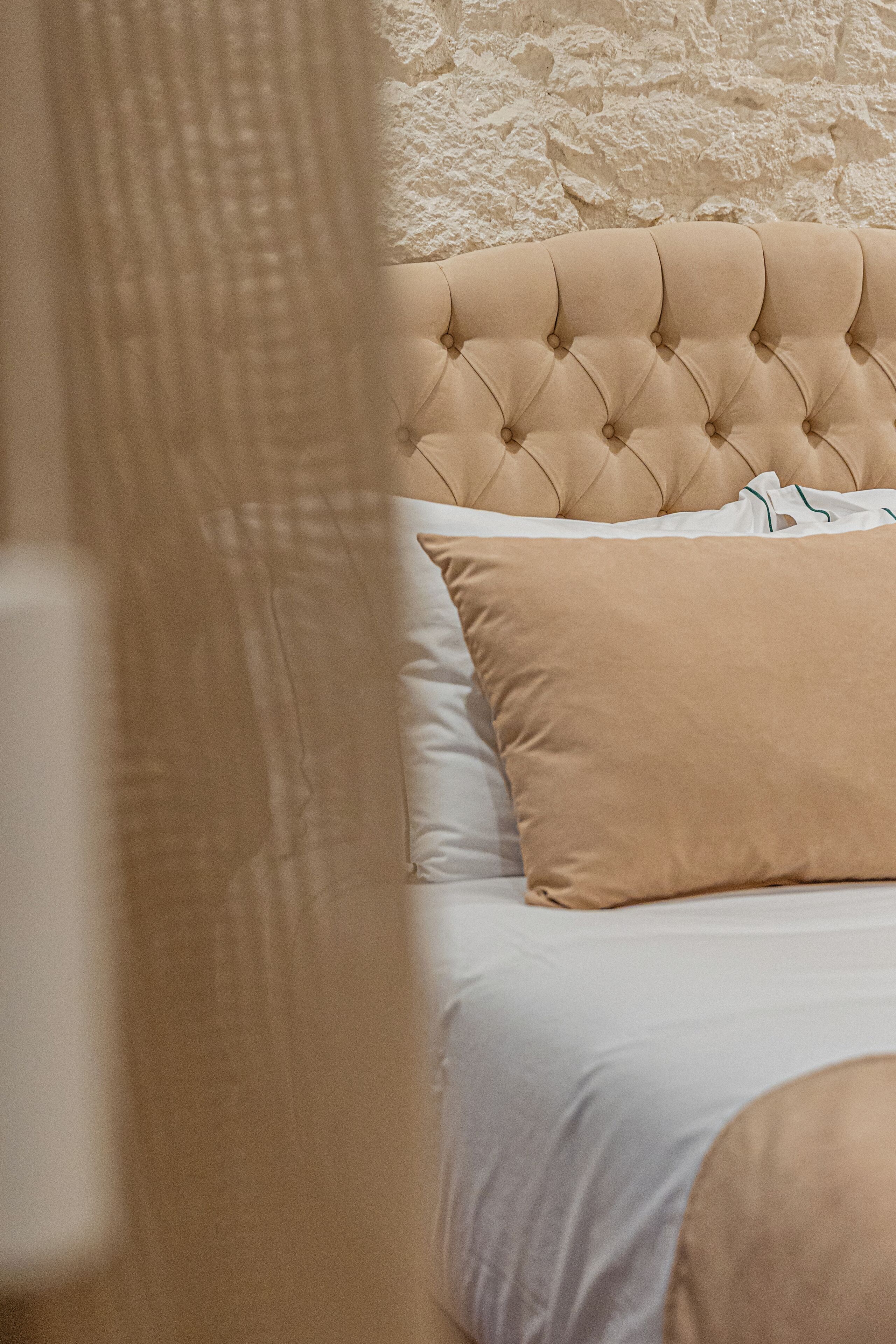 Uma cama com cabeceira estofada, roupa de cama branca e travesseiro bege.