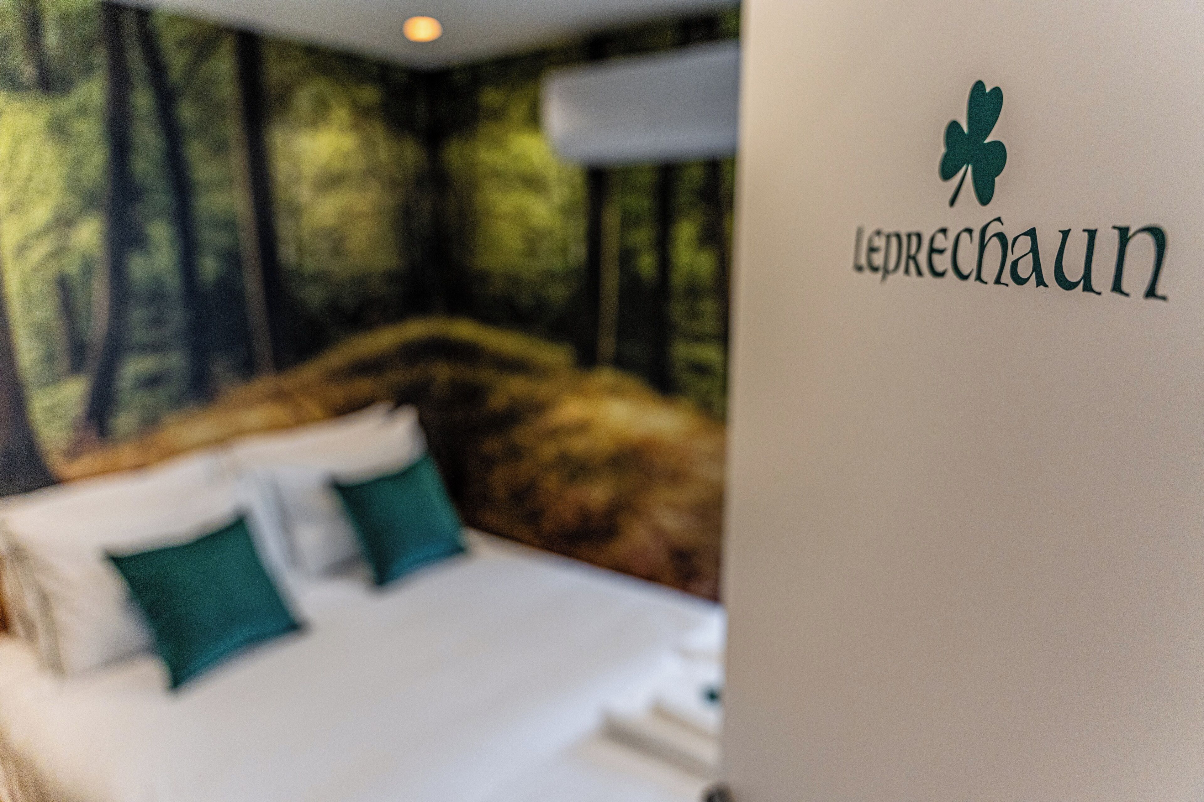 A bed with green pillows and a wall with a forest mural.