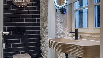 Un baño con piso de diseño blanco y negro, un espejo redondo con luz, un lavamanos y un inodoro.