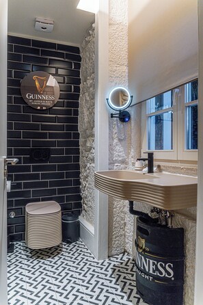 A bathroom with a black and white patterned floor, a round mirror with a light, a sink, and a toilet. - Celtic Lodge (Viseu)