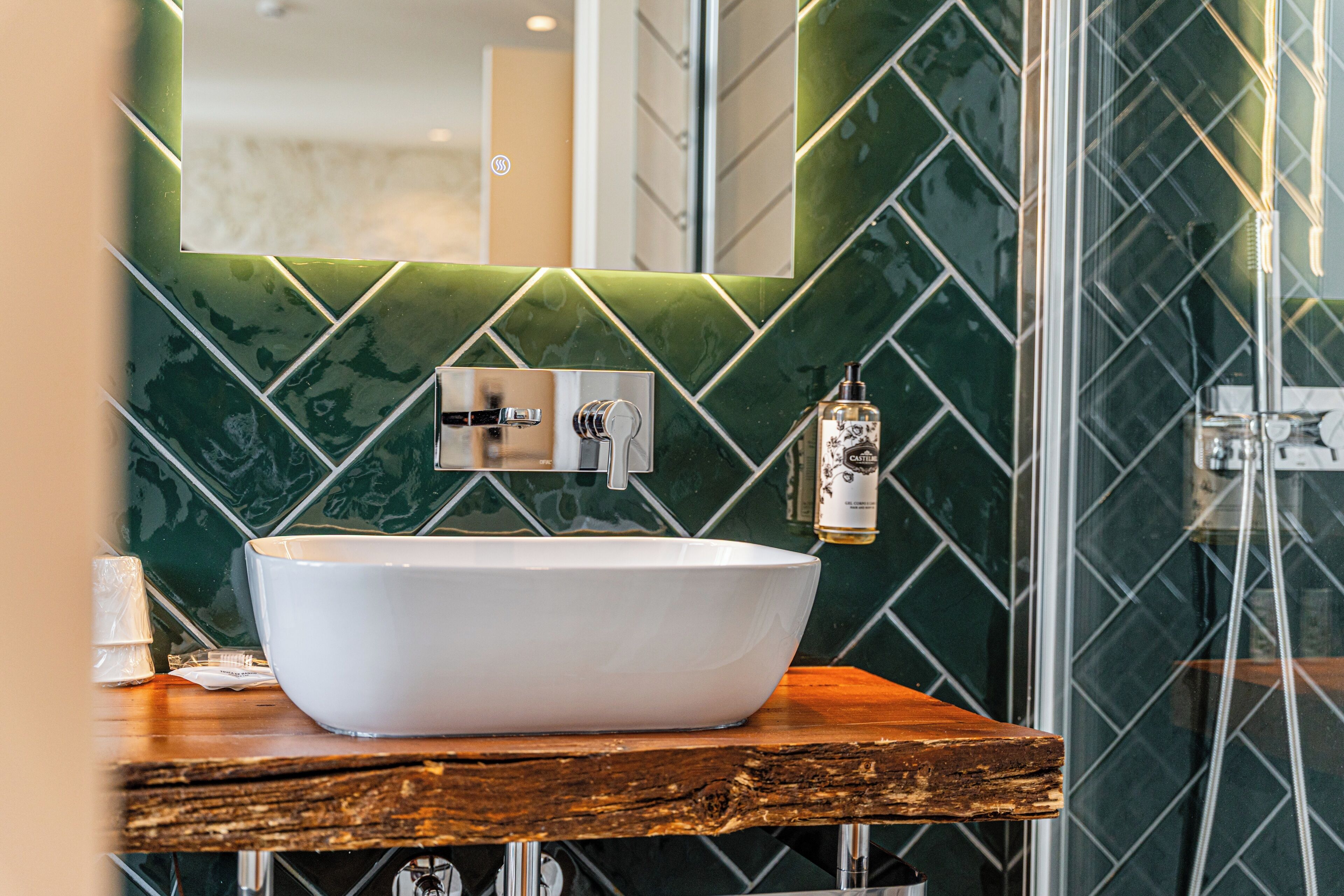 Un baño con un lavamanos blanco tipo recipiente, una encimera de madera y un salpicadero con azulejos verdes.