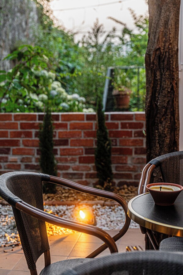A patio with wicker chairs, a table with a candle, and a brick wall with greenery. - Celtic Lodge (Viseu)
