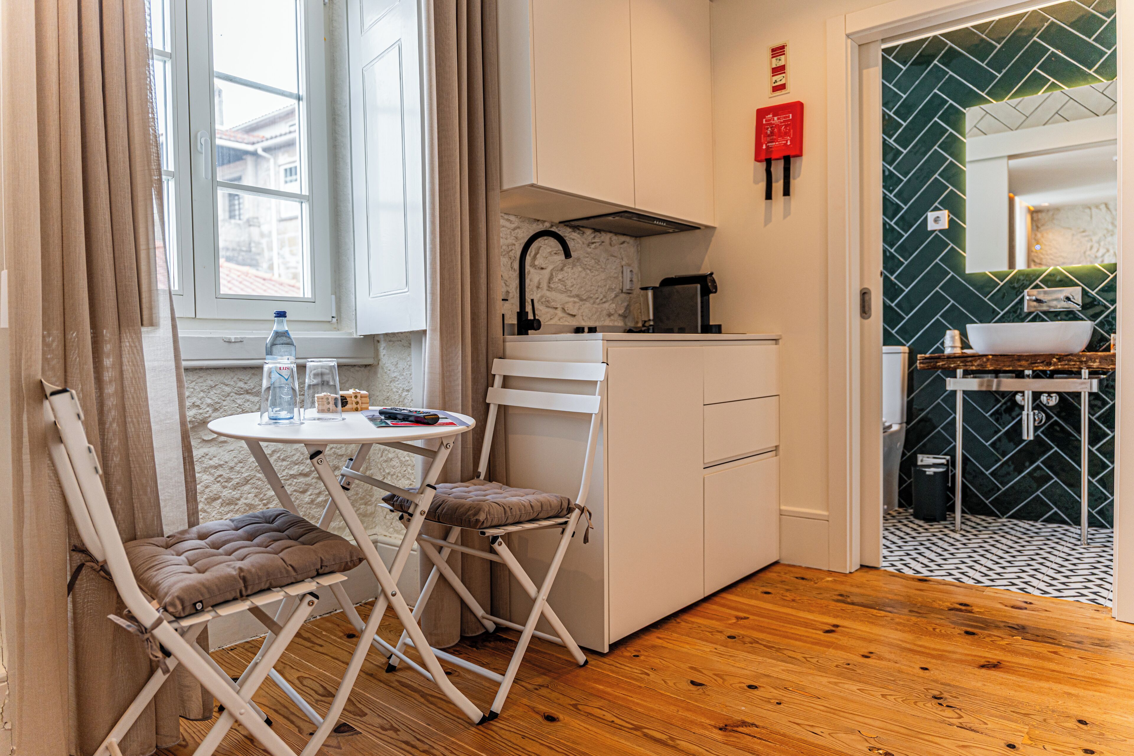 Cozinha compacta com área de refeições, incluindo uma mesa com cadeiras, bancada pequena e janela com cortinas.