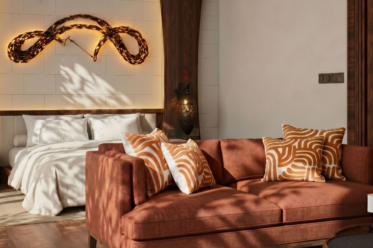 A modern living room with a sofa, patterned cushions, a decorative wall light, and a bed with white bedding.