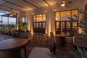 A spacious outdoor seating area with wooden tables and chairs, surrounded by large windows and potted plants. - Avala Nusa Dua, Bali, a Tribute Portfolio Resort (Nusa Dua)