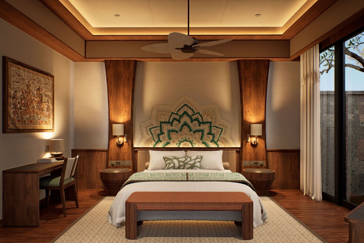 A bedroom with a large bed, two bedside tables, a desk, a chair, a bench, a ceiling fan, and a large wall tapestry.