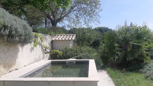 Une piscine dotée d’une terrasse carrelée, entourée de verdure et bordée d’un bâtiment dont le toit est également recouvert de tuiles.