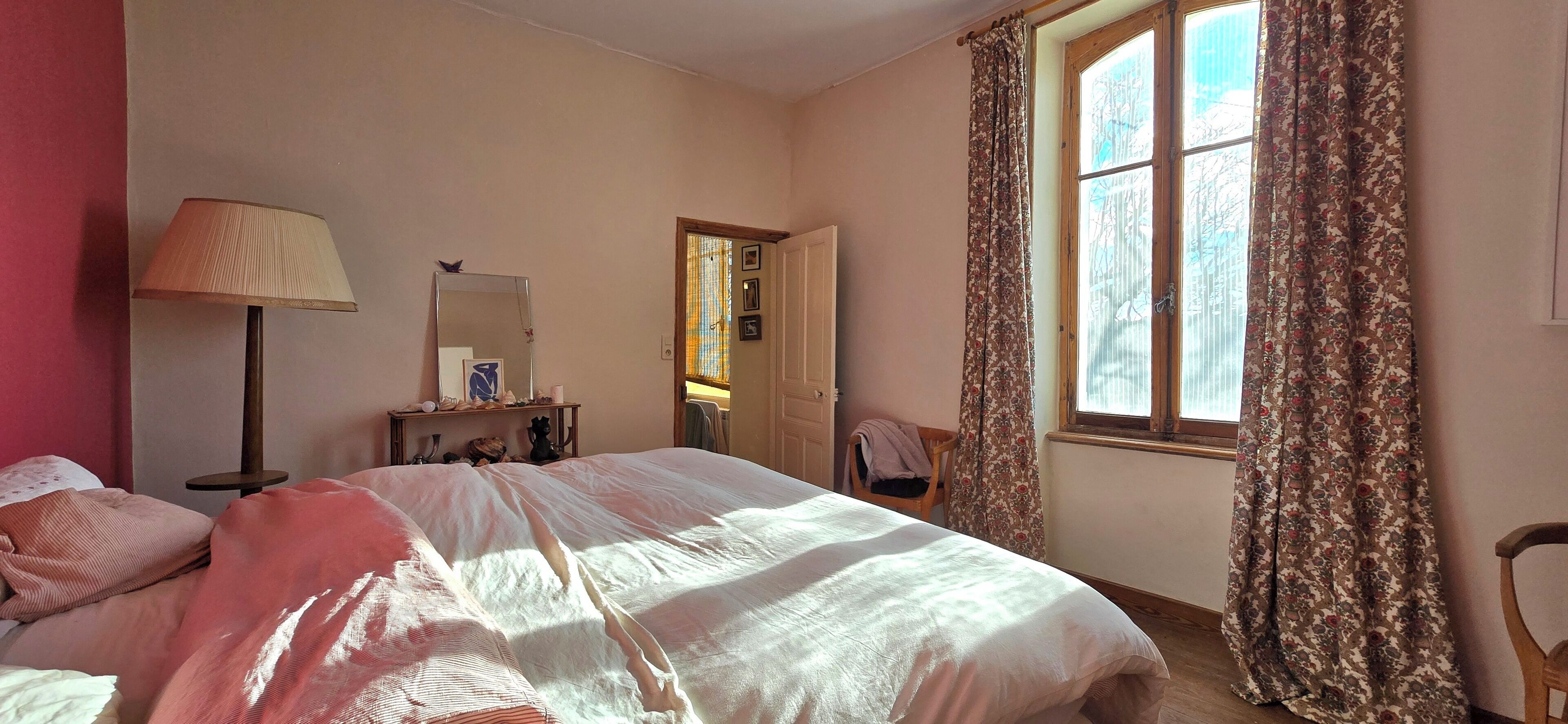 A bedroom with a bed, a bedside table, a lamp, a chair, and a window with curtains.
