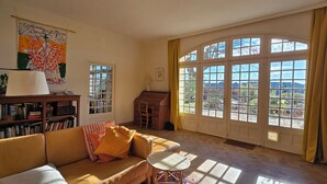 Un salon confortable avec un canapé, une petite table, une bibliothèque et une grande fenêtre avec des rideaux.
