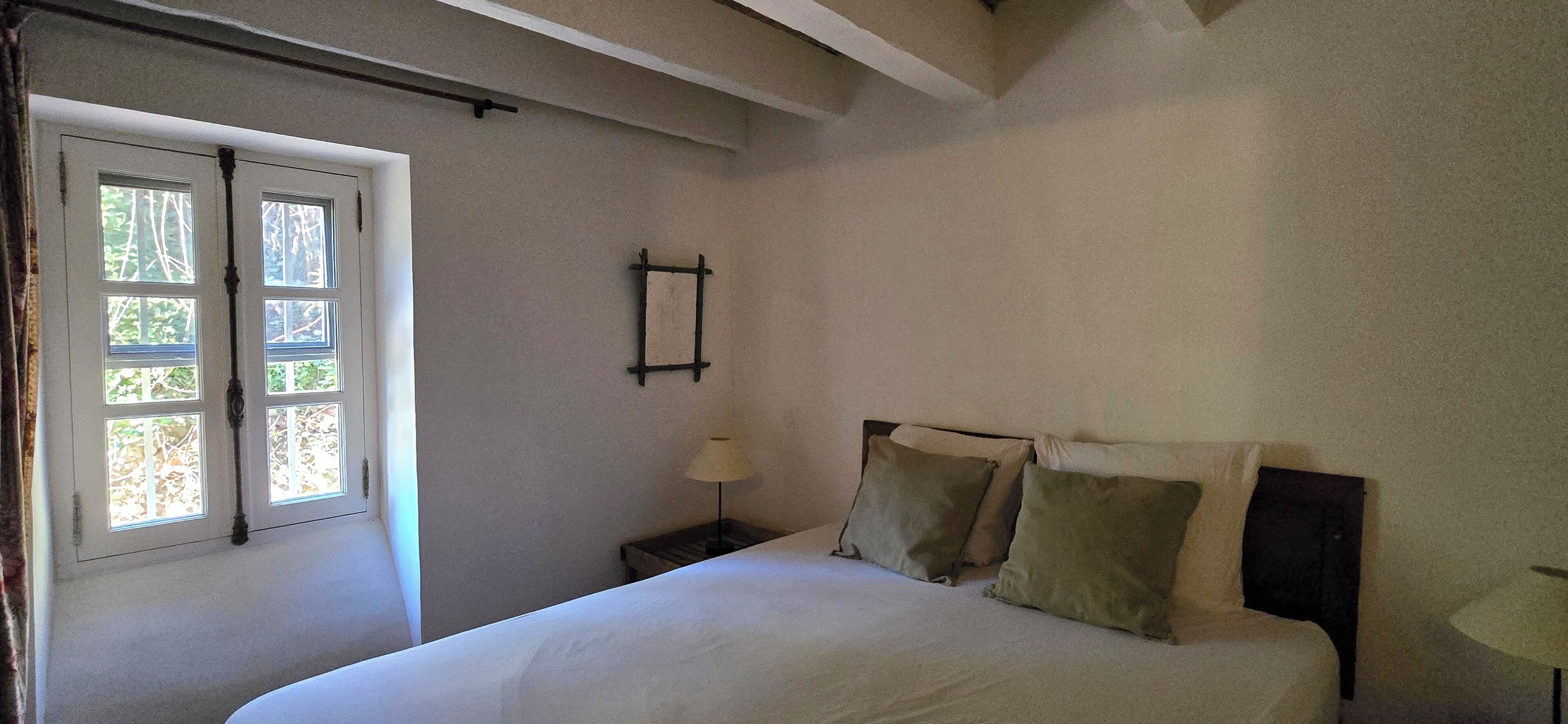 Une chambre à coucher avec un lit, une table de chevet, une lampe et une fenêtre avec des rideaux.