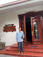 A person standing in front of a house with a wooden door and a sign that reads "HAAP VIET TRAVEL".