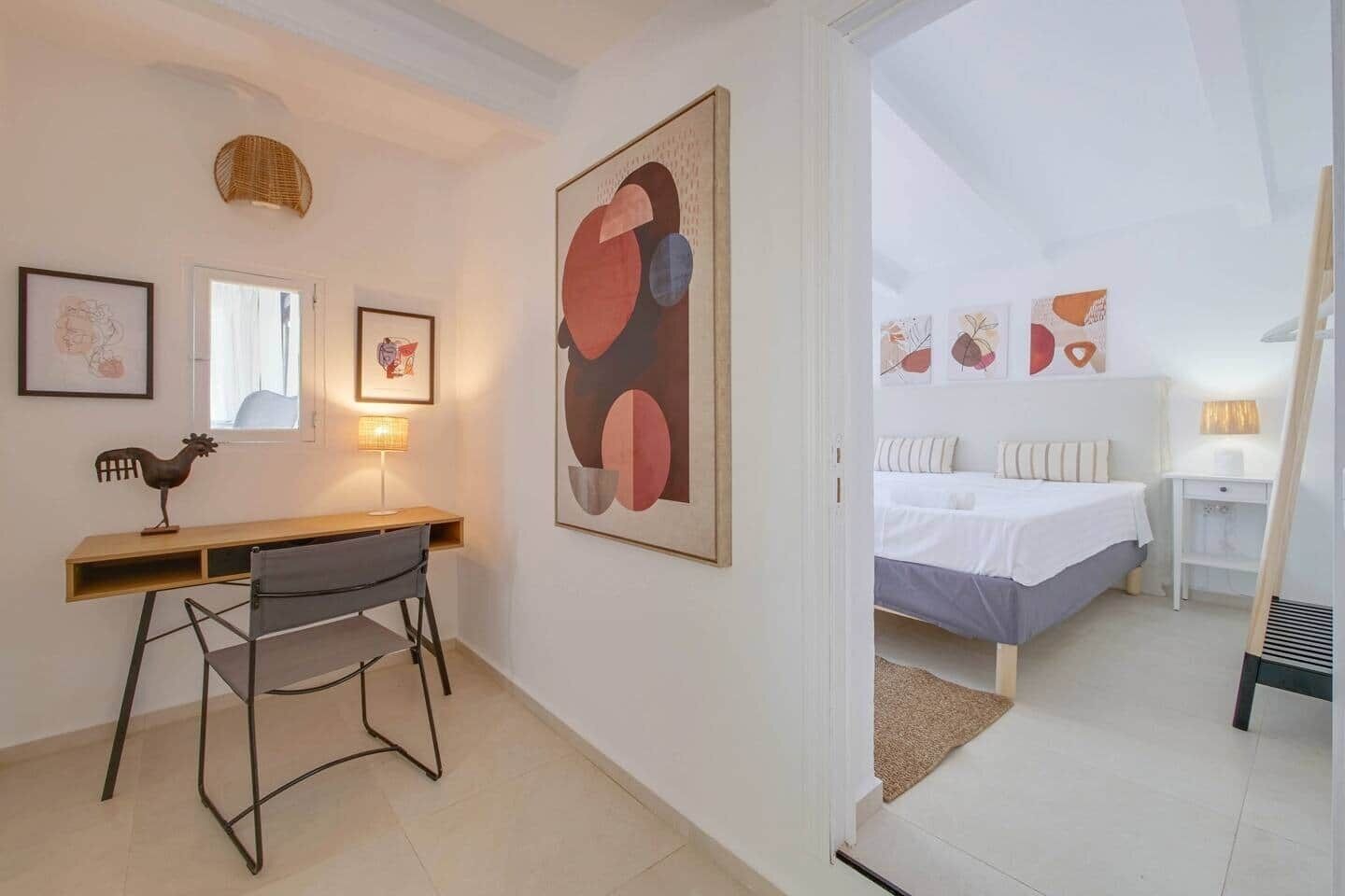 A room with a bed, a desk, a chair, a lamp, and a painting on the wall.