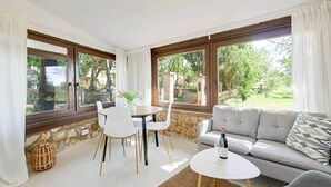 A room with a sofa, a dining table with chairs, a small round table with a bottle, and large windows with curtains. - Casita - XXL Pool, Nature, Yoga, AC (AG/6) (Manacor)