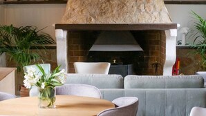 Un soggiorno moderno con camino in pietra, sedute rivestite di grigio, un tavolino rotondo in legno e un vaso con fiori bianchi.