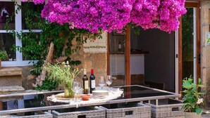 Zona pranzo all'aperto con mobili in vimini, un tavolo apparecchiato con bicchieri da vino, piatti e una bottiglia.