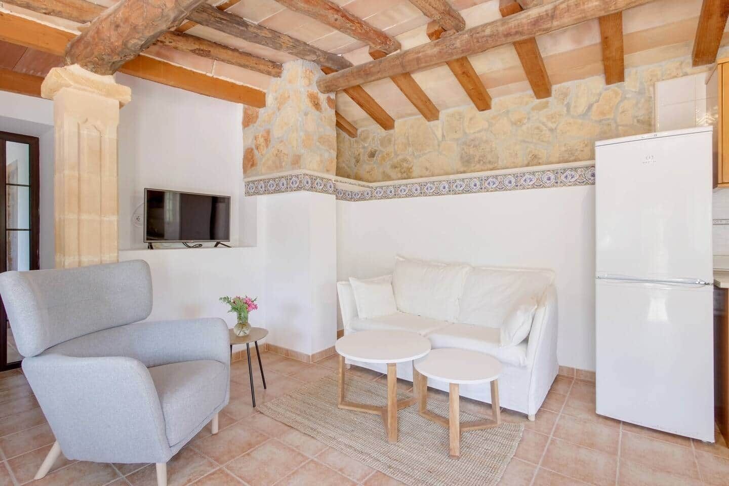 A cozy living room with a stone wall, a white sofa, a grey armchair, a small table, and a white refrigerator.