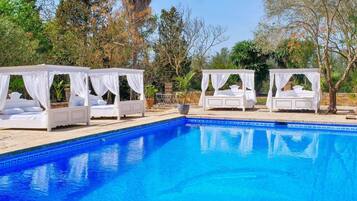 Un espace piscine agrémenté de quatre lits à baldaquin blancs disposés autour.