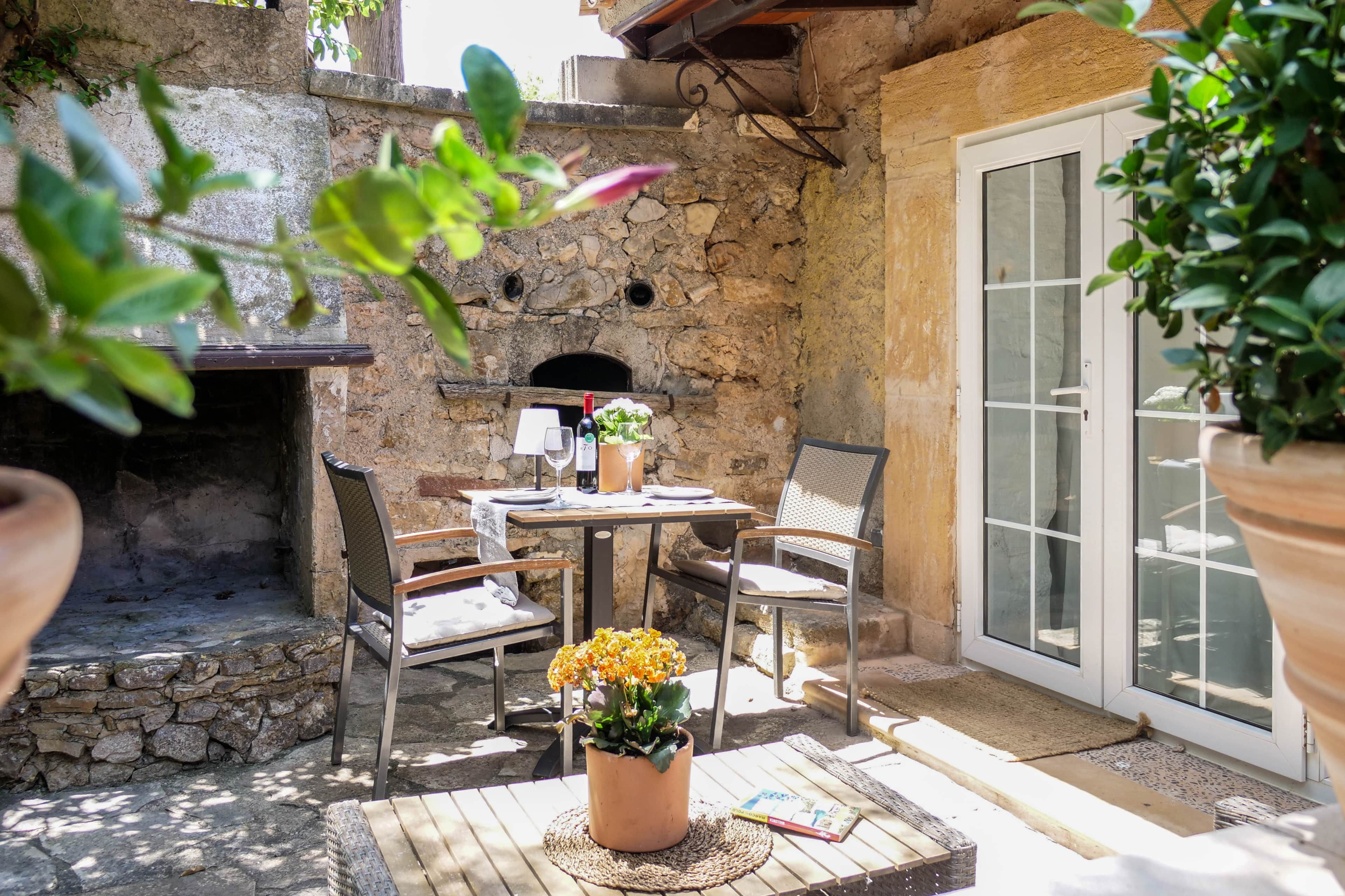 Une terrasse extérieure avec des murs en pierre, une table avec des chaises, une plante en pot et un livre.