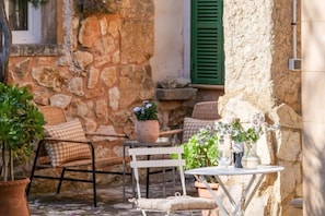 Un mur de pierre, une chaise blanche, une petite table et une plante en pot.