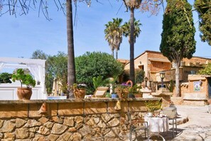 A stone wall with potted plants, a white canopy, and a table with chairs outside a building.