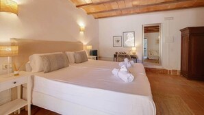 Een slaapkamer met een groot bed, houten balken in het plafond, een nachtkastje met een lamp en een spiegel.