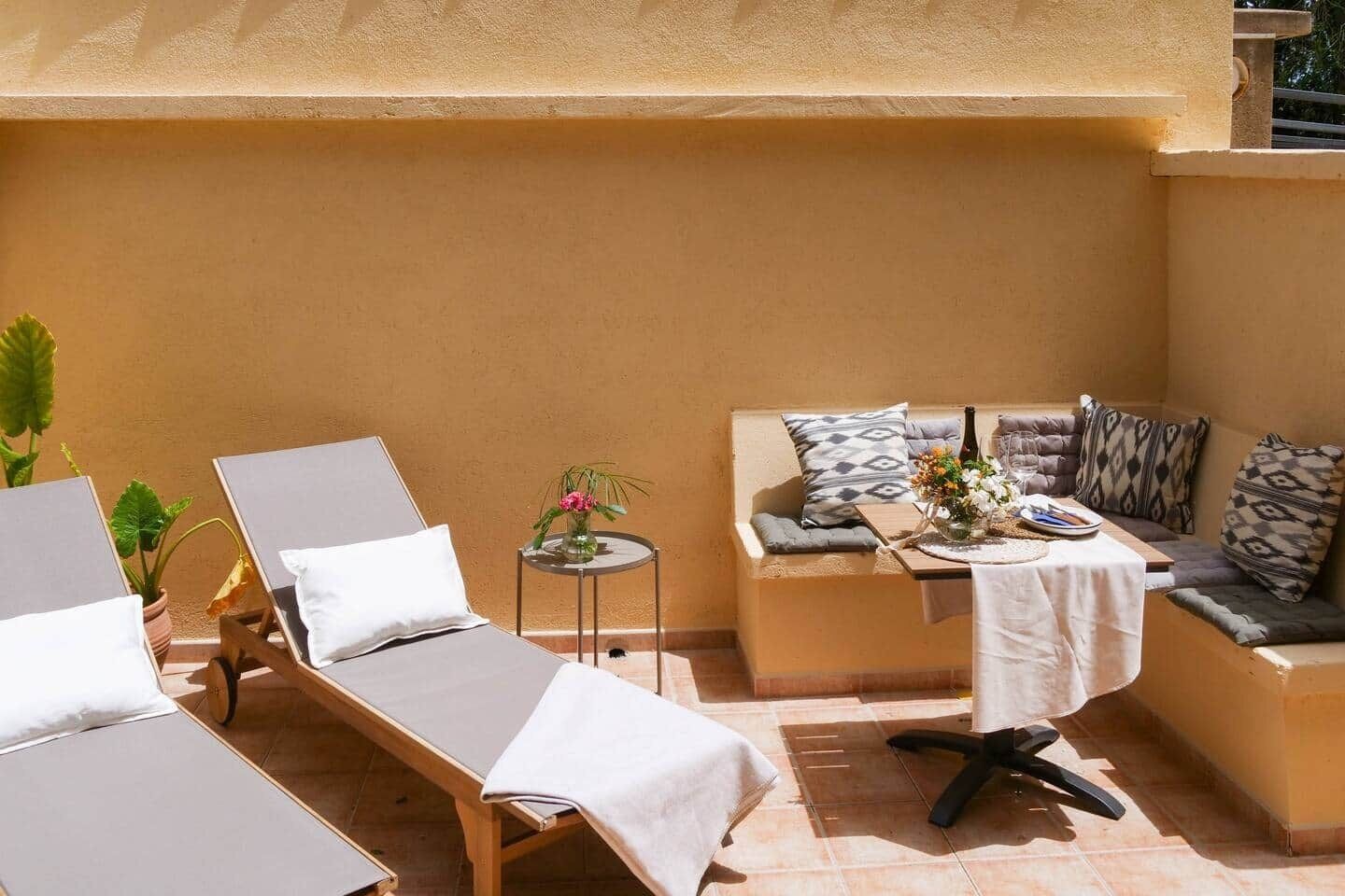 Ein sonniger Außenbereich mit Lounge-Möbeln, einer Sitzecke und einem kleinen Tisch mit Blumen.
