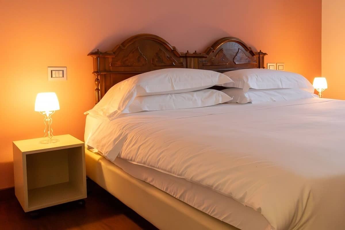 Un letto rifatto con lenzuola bianche, due abat-jour e una testiera in legno.