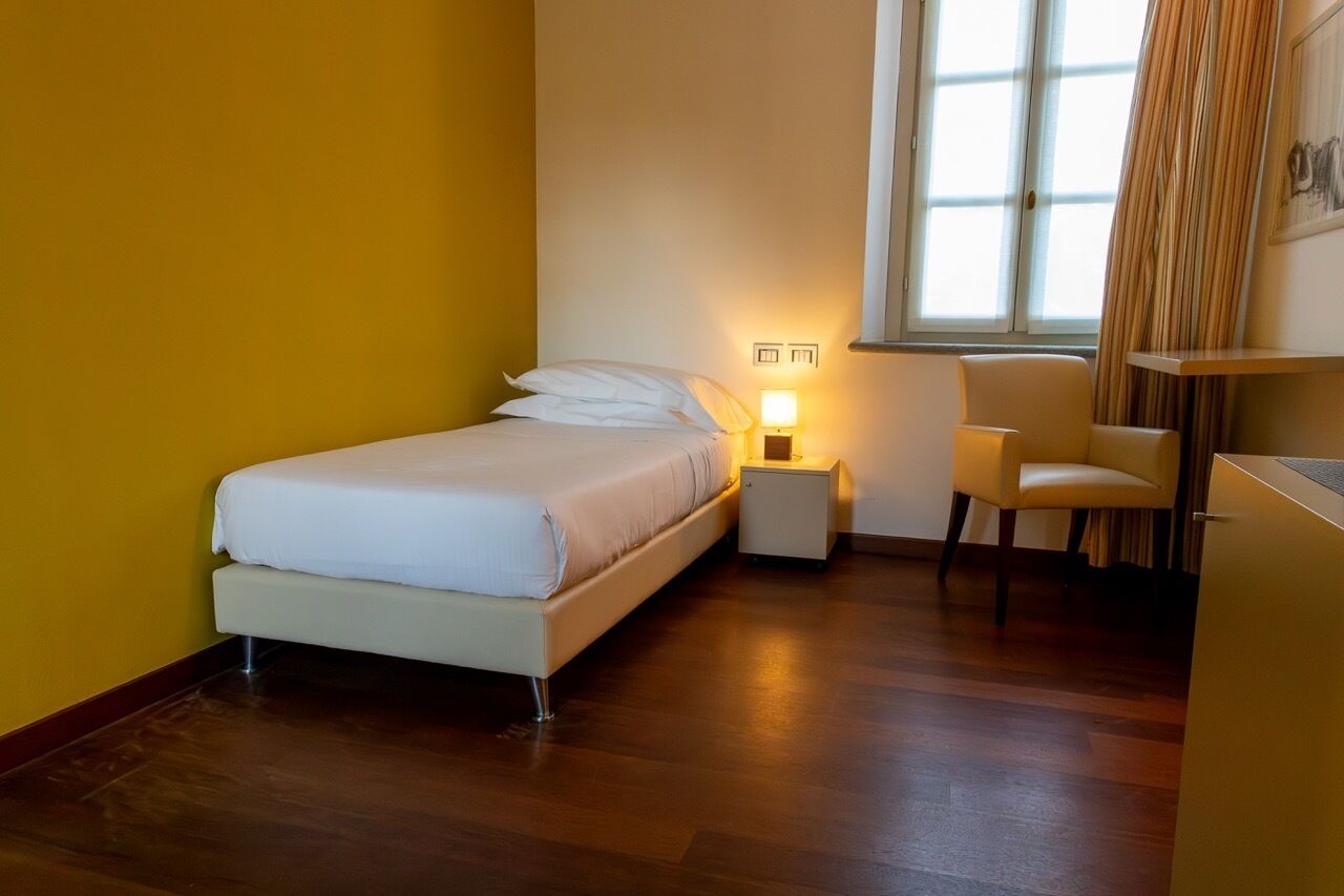 Un dormitorio con cama, mesita de noche, silla y ventana con cortinas.