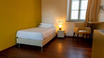 Un dormitorio con cama, mesita de noche, silla y ventana con cortinas.