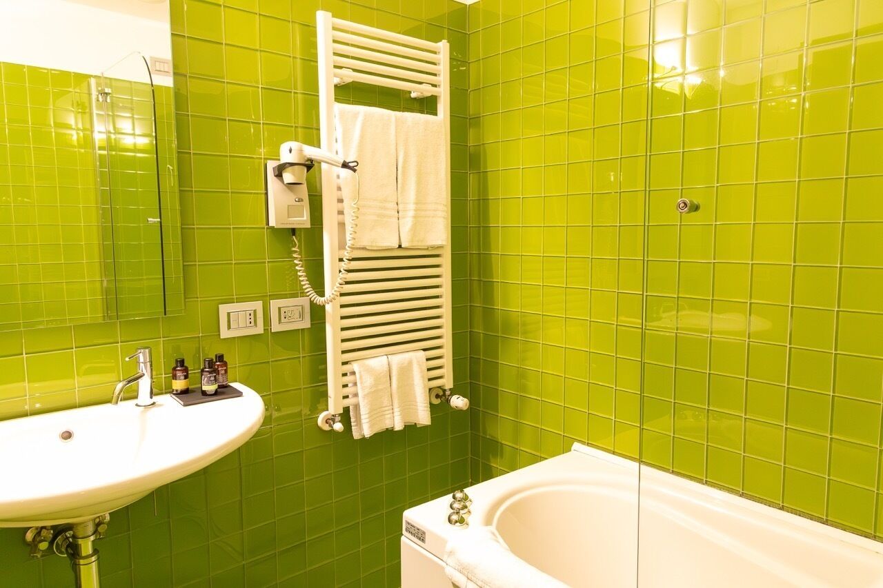 A bathroom with green tiles, a white sink, a white bathtub, and a towel rack with towels.