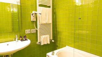 Un baño con azulejos verdes, un lavamanos blanco, una bañera blanca y un perchero con toallas.
