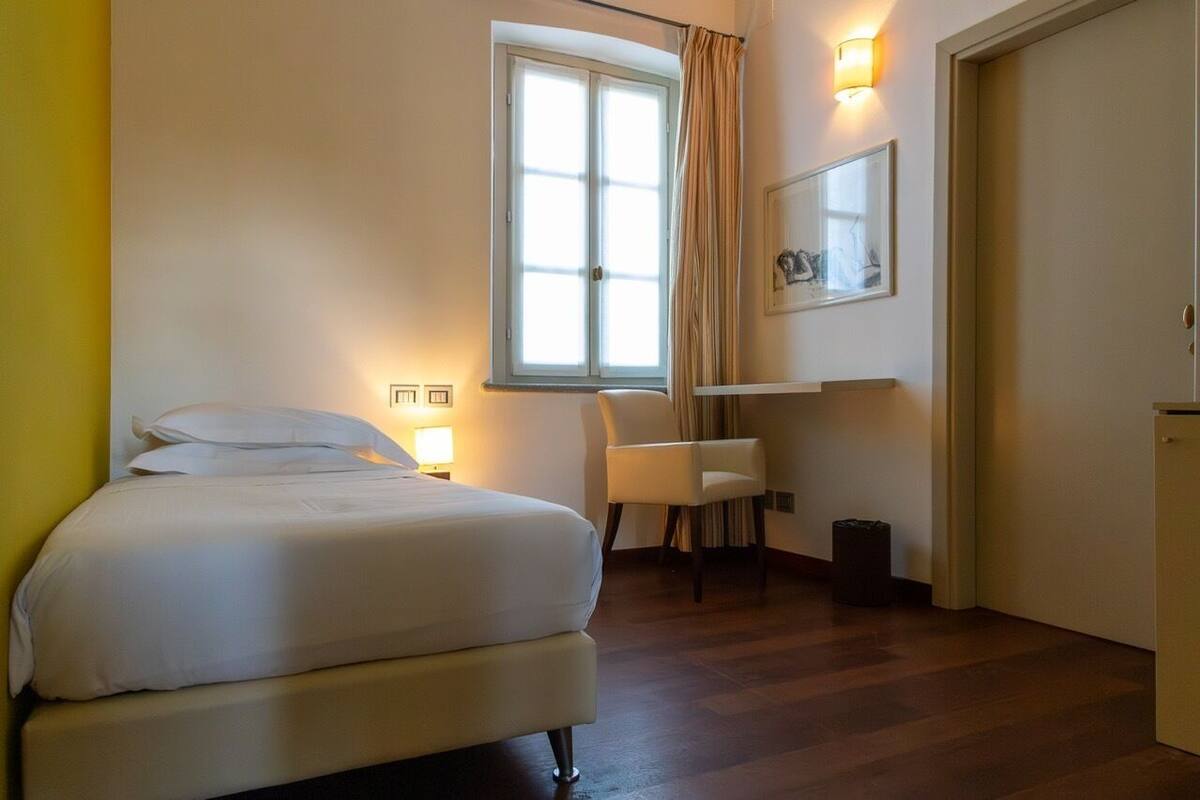 Una camera d'albergo con un letto, una sedia, una scrivania, una finestra e una porta.