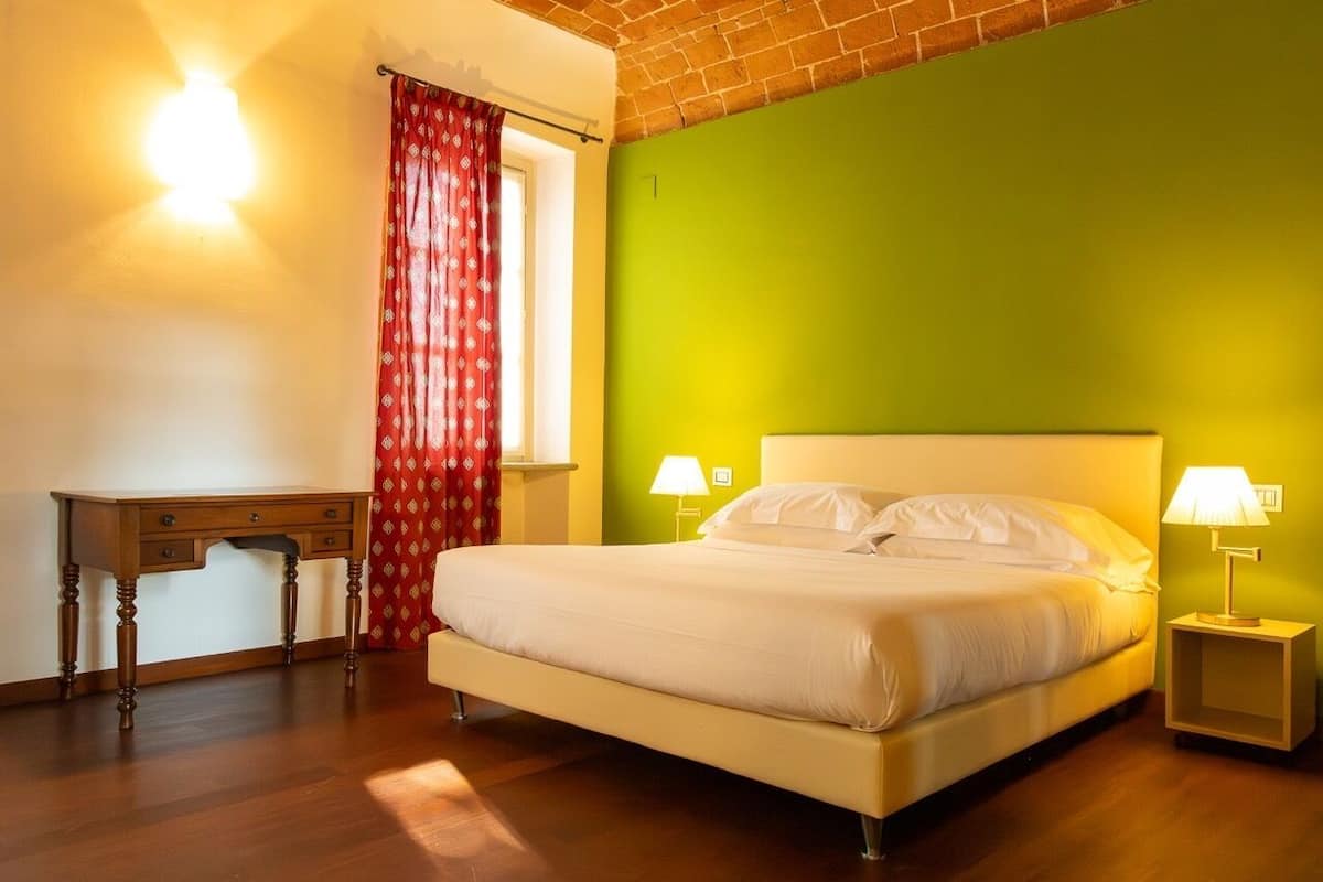 Un letto con due abat-jour, una scrivania in legno e una tenda rossa.