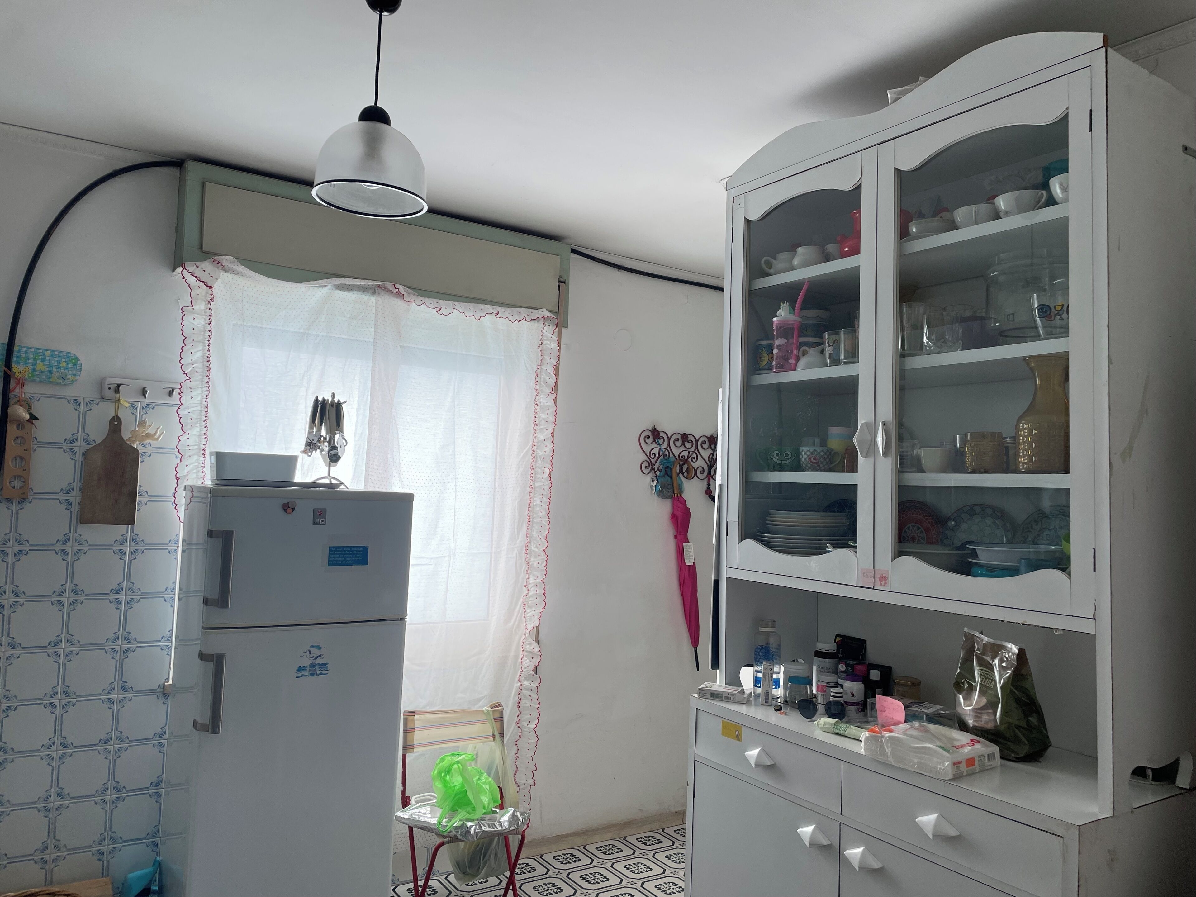 A kitchen with a refrigerator, a cabinet with glass doors, and a hanging light fixture.