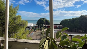 A view from a window overlooking a beach with a clear sky, palm trees, and a building with a red roof. - Comfortable house with terrace a stone's throw from the sea in mild climate location (Villapiana Lido)