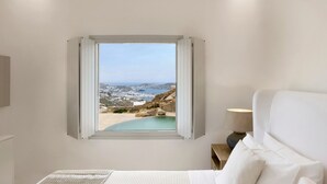 Ein Schlafzimmer mit großem Fenster und Blick auf eine Küstenlandschaft, einem Bett, einem Nachttisch mit Lampe und einem Pool.