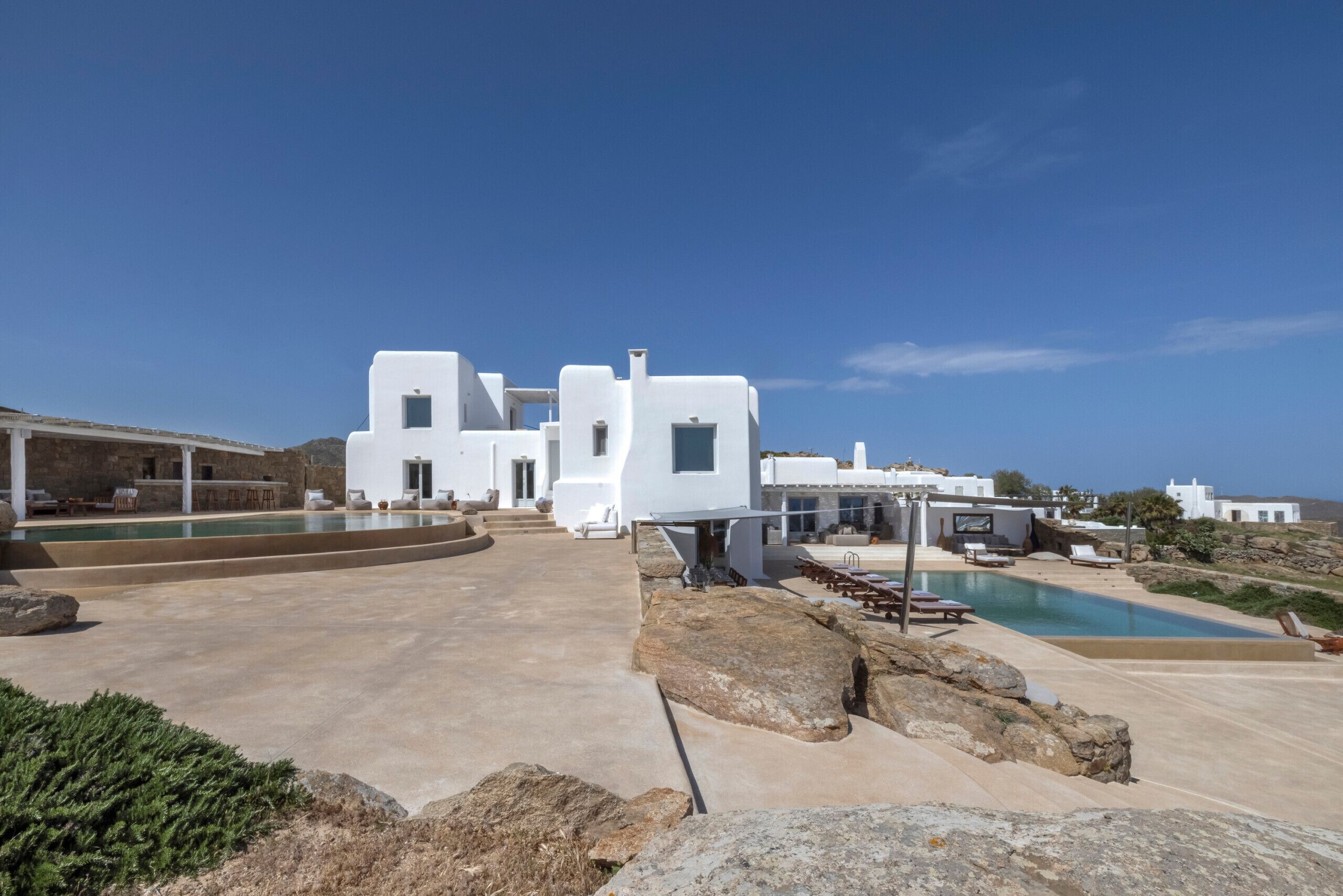 A modern white villa with a pool, outdoor seating, and a view of the sea.