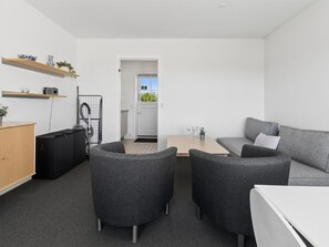 Ett modernt, minimalistiskt vardagsrum med en soffa, två fåtöljer, ett litet bord och ett skåp.
