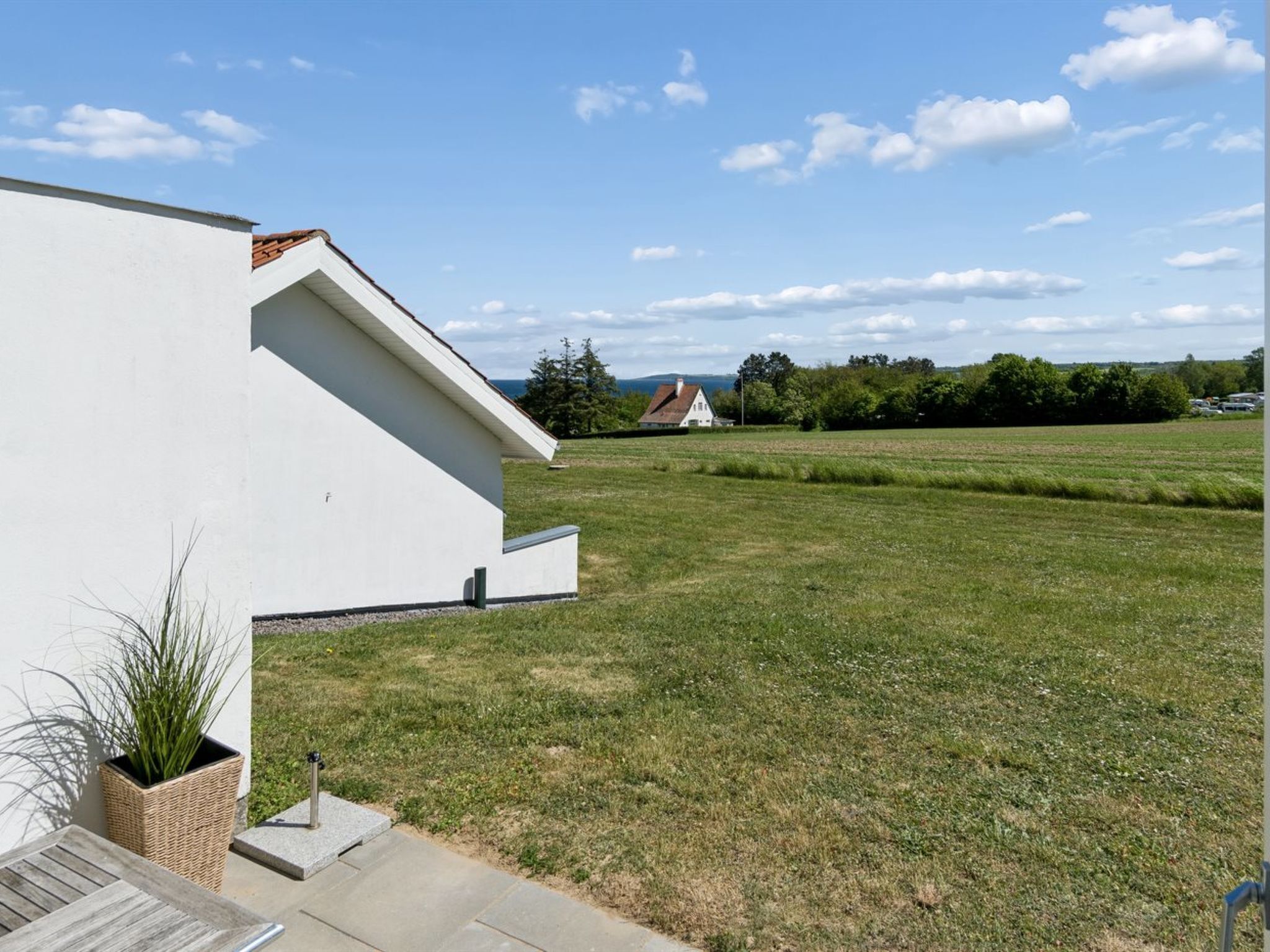 Ein modernes Gebäude mit flachem Dach, einem grünen Hof und weiter Aussicht auf ein Haus und Bäume.