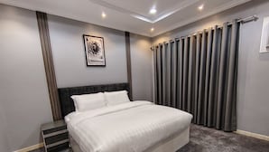 Moderni hotellihuone, jossa on suuri sänky, pääty, seinälle kiinnitetty taideteos ja ikkuna, jossa on verhot.