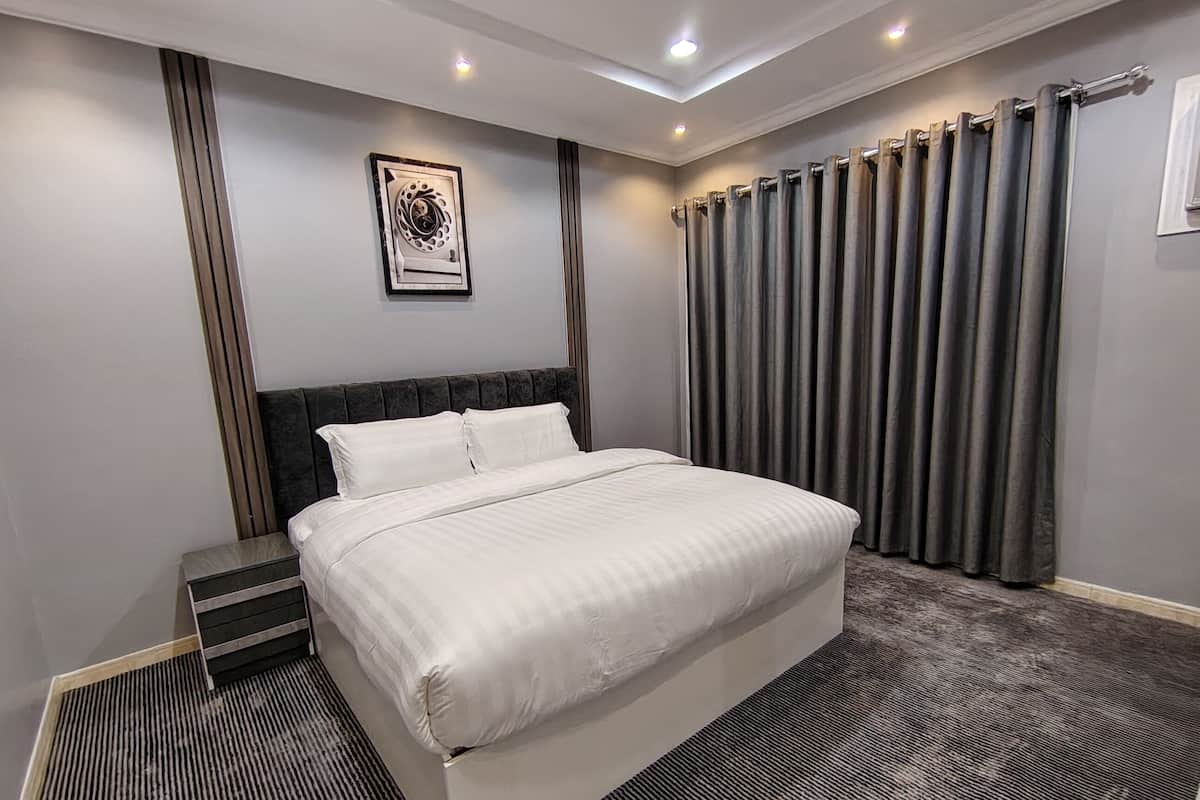 Ein modernes Hotelzimmer mit einem großen Bett, einem Kopfteil, einem Wandbild und einem Fenster mit Vorhängen.