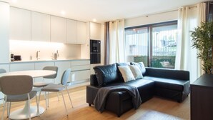 Ein modernes Wohnzimmer mit einer schwarzen Ledersofa, einem Esstisch mit Stühlen und einer Küchenzeile mit weißen Schränken und einem eingebauten Backofen.