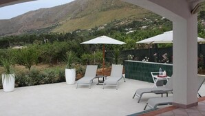 Eine Außenpatio mit weißen Lounge-Stühlen und Sonnenschirmen, umgeben von Topfpflanzen und Blick auf eine Berglandschaft.