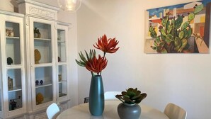 Ein Essbereich mit einem weißen Tisch, zwei Vasen mit Pflanzen, einem weißen Schrank mit Glastüren und einem Gemälde an der Wand.