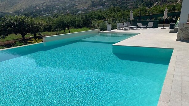 Ein rechteckiger Swimmingpool mit klarem, blauem Wasser, umgeben von einer gefliesten Liegefläche und Liegestühlen.