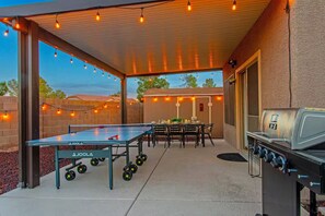Une terrasse extérieure équipée d’une table de ping-pong, d’un barbecue et de guirlandes lumineuses.