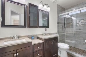 Une salle de bain moderne avec deux vasques, des meubles en bois foncé et une cabine de douche en verre.